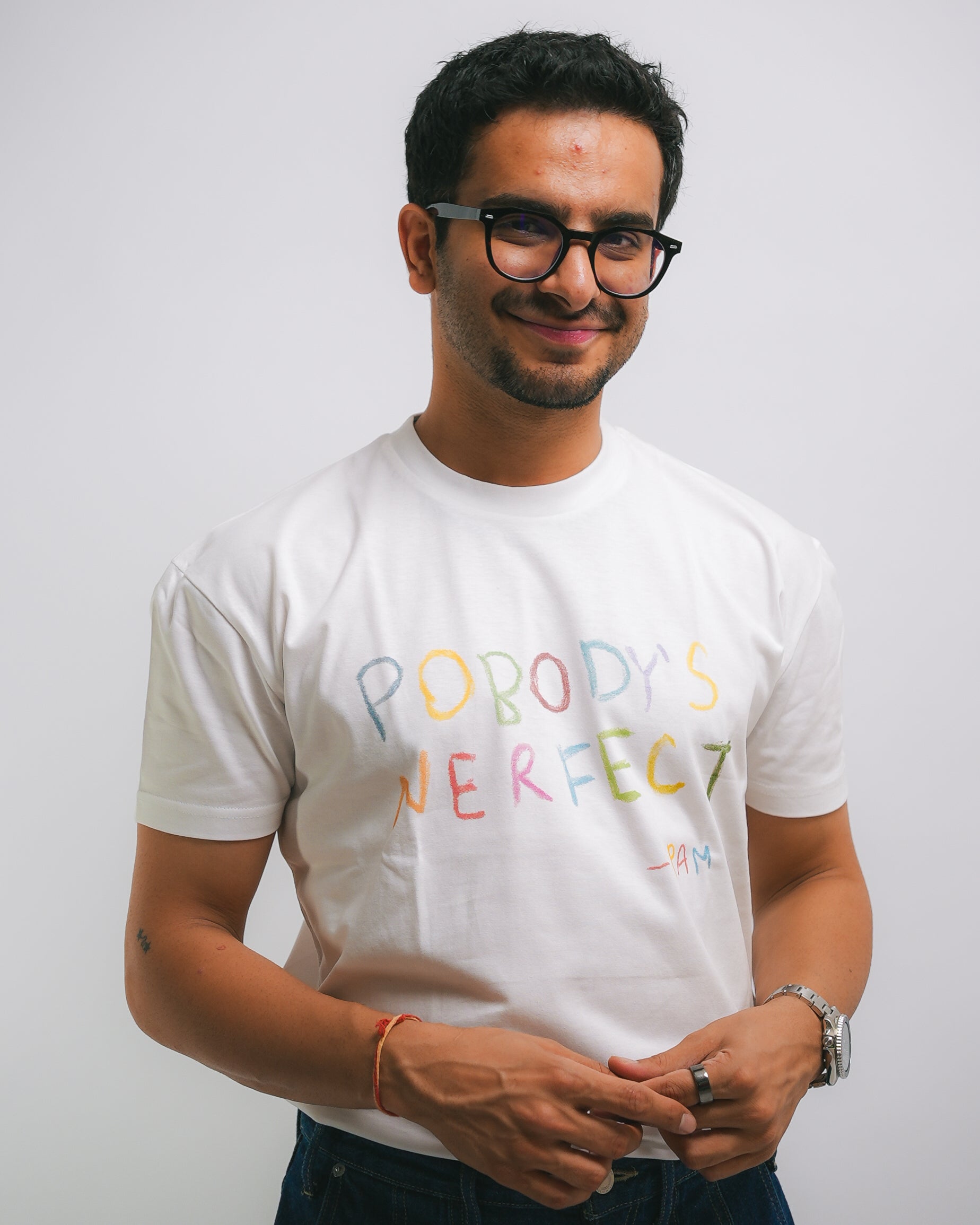A man wearing a white graphic t-shirt with the text 'PABODY'S PERFECT' printed in a colorful, hand-drawn style. The background is a clean, neutral light gray studio backdrop.